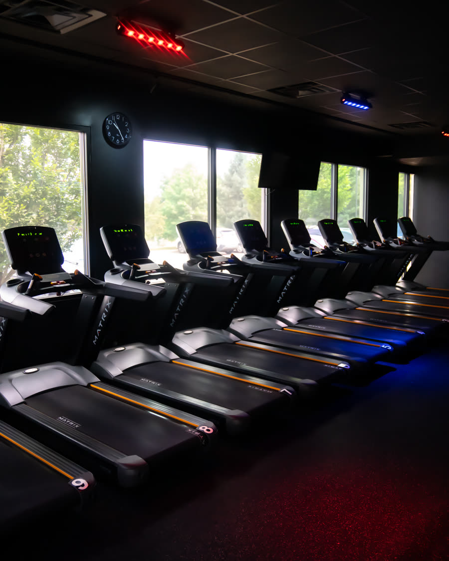 A row of treadmills along the studio windows under red and blue lighting