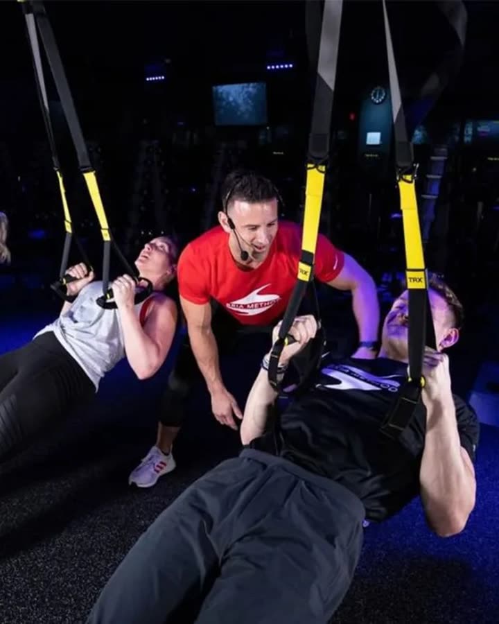 A Bria Method coach guiding two members through a TRX suspension exercise